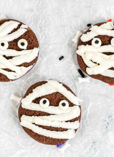Three chocolate cookies close up decorated with frosting and candy eyes to look like mummies