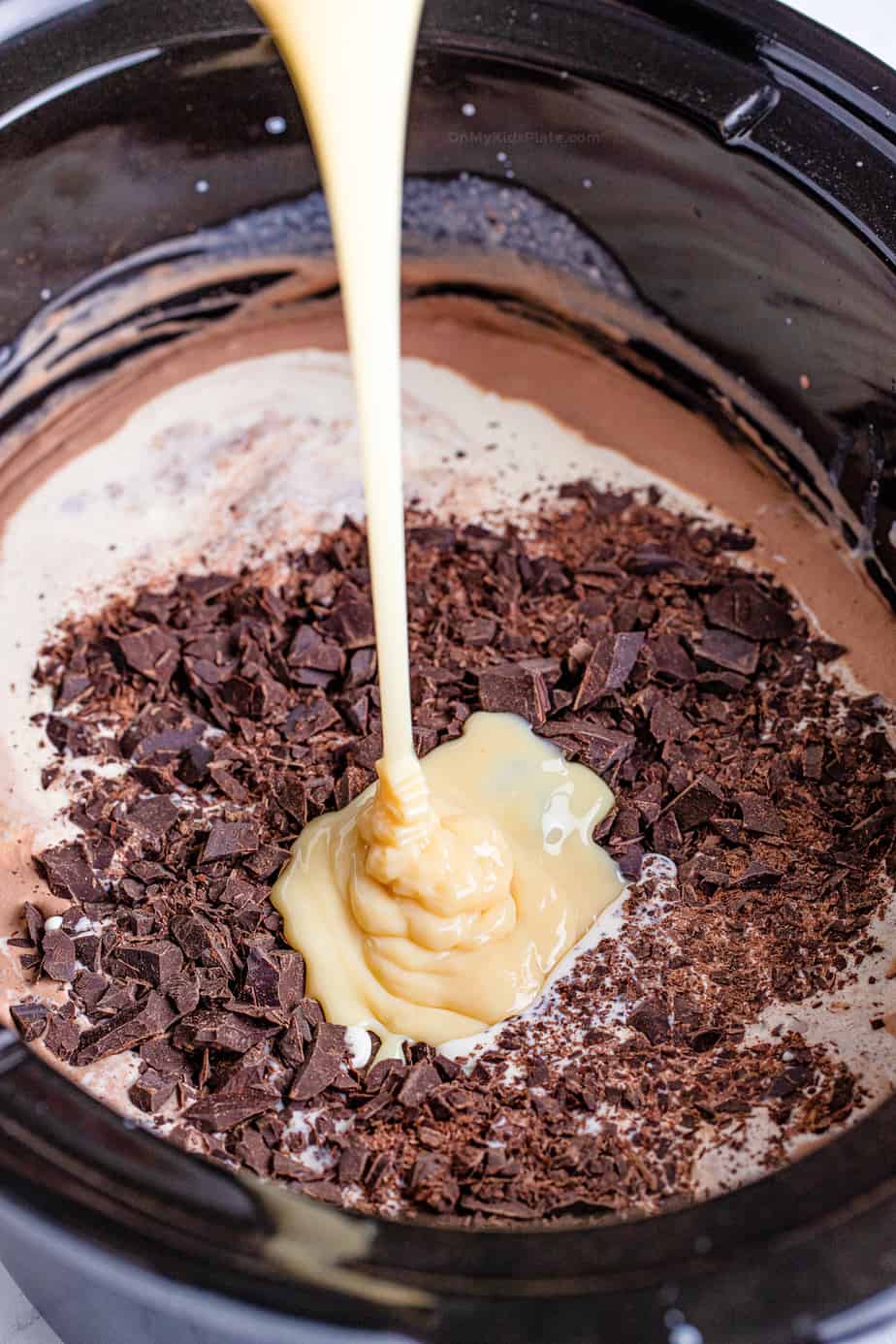 Pooring condensed milk into slow cooker on top of chopped chocolate