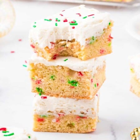 Three frosted sugar cookie bars stacked and covered with sprinkles. Top bar is missing a bite.