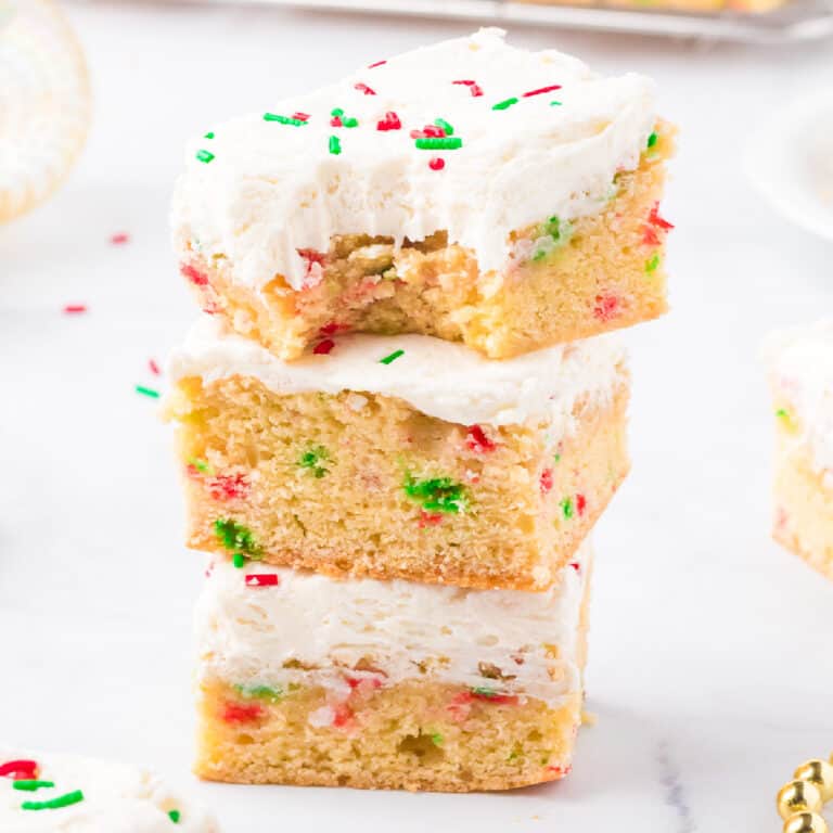 Three frosted sugar cookie bars stacked and covered with sprinkles. Top bar is missing a bite.