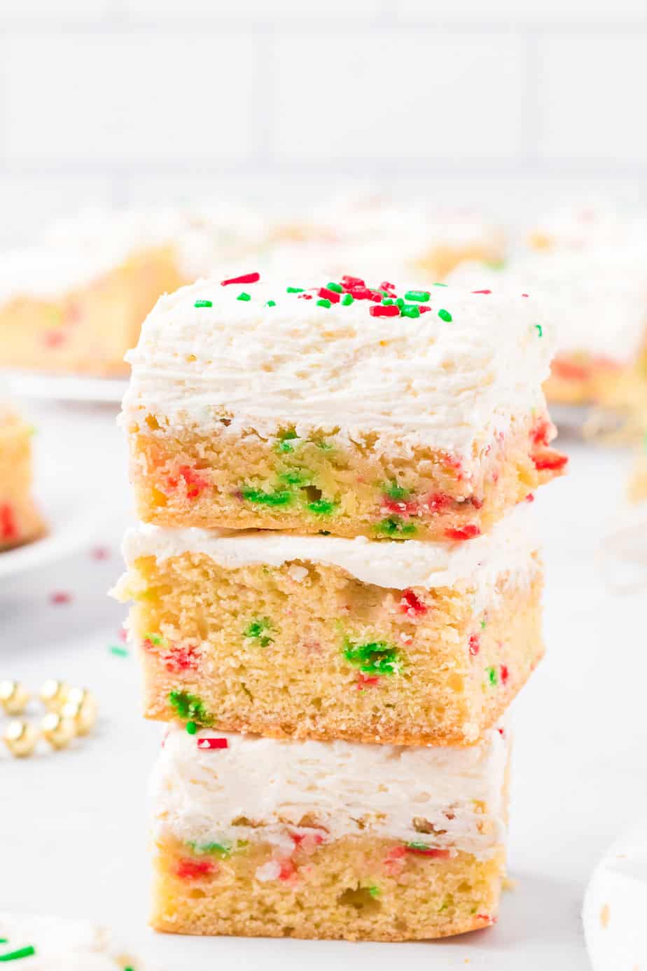 Sugar cookie bars frosted and full of red and green sprinkles stacked three bars high from the side on a counter.