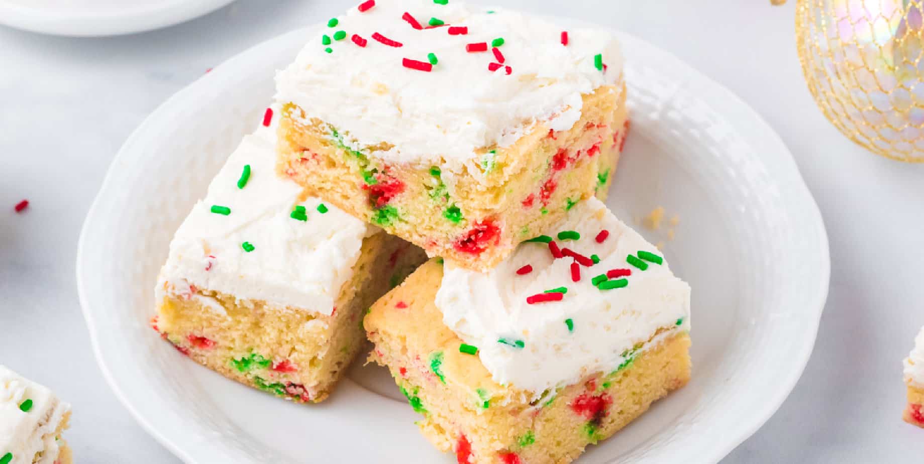 Christmas sugar cookie bars stacked on a plate from the side with sprinkles.