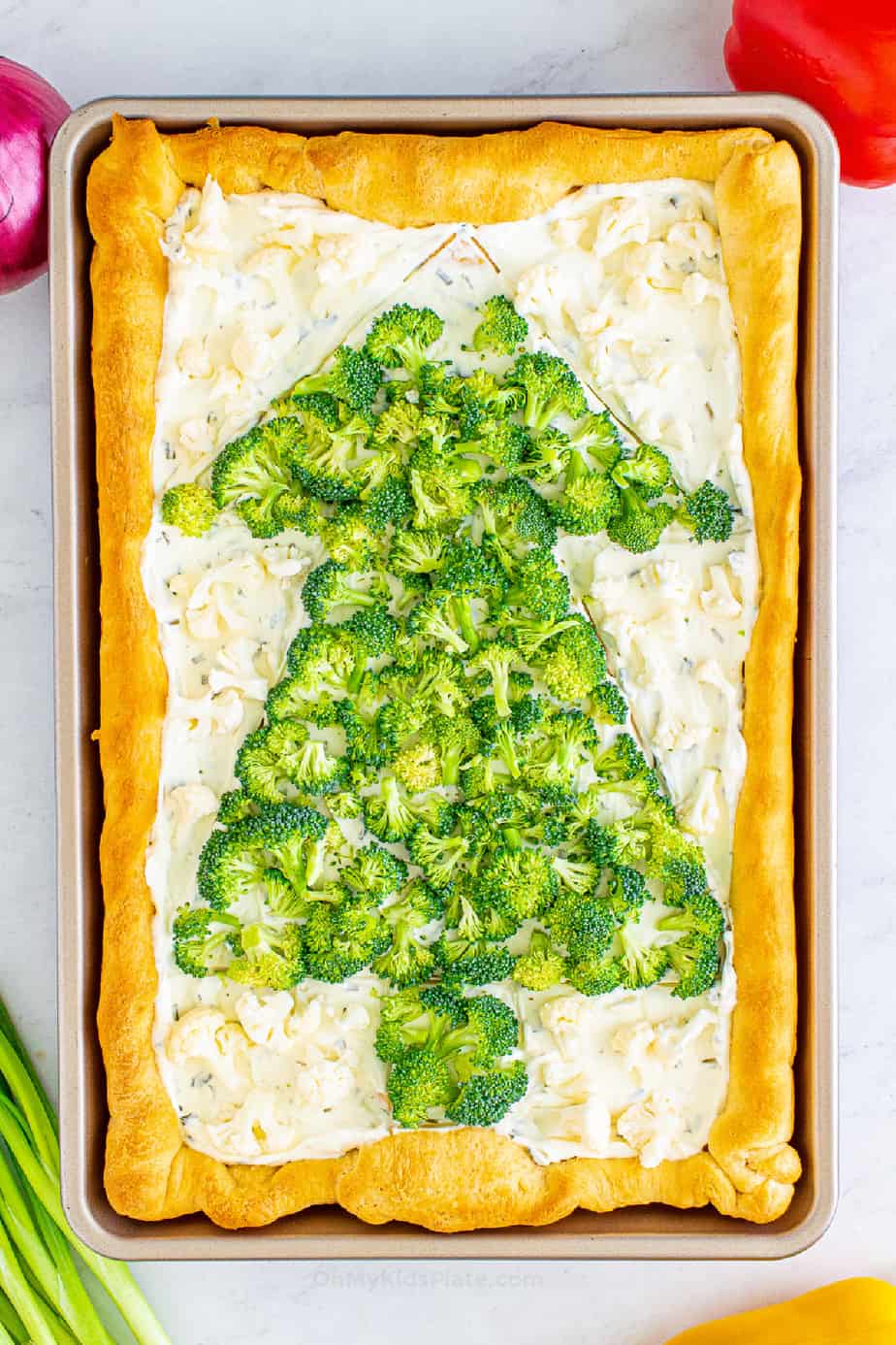 Decorating the Christmas tree on the veggie pizza with broccoli and cauliflower for the white spaces. from overhead