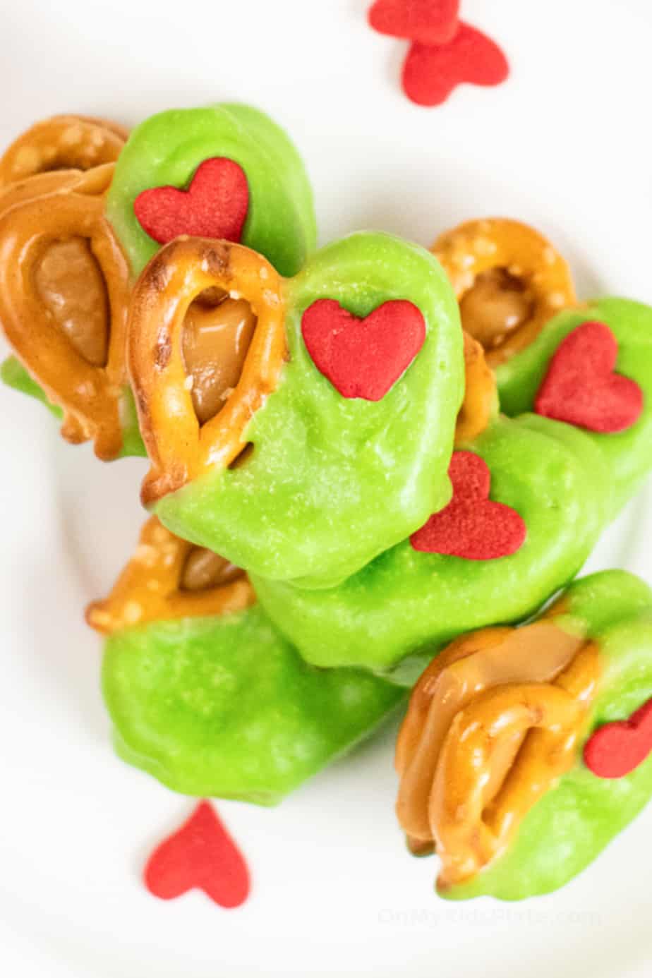 Close up of a stack of pretzels and caramel candies covered in green chocolate with red hearts.