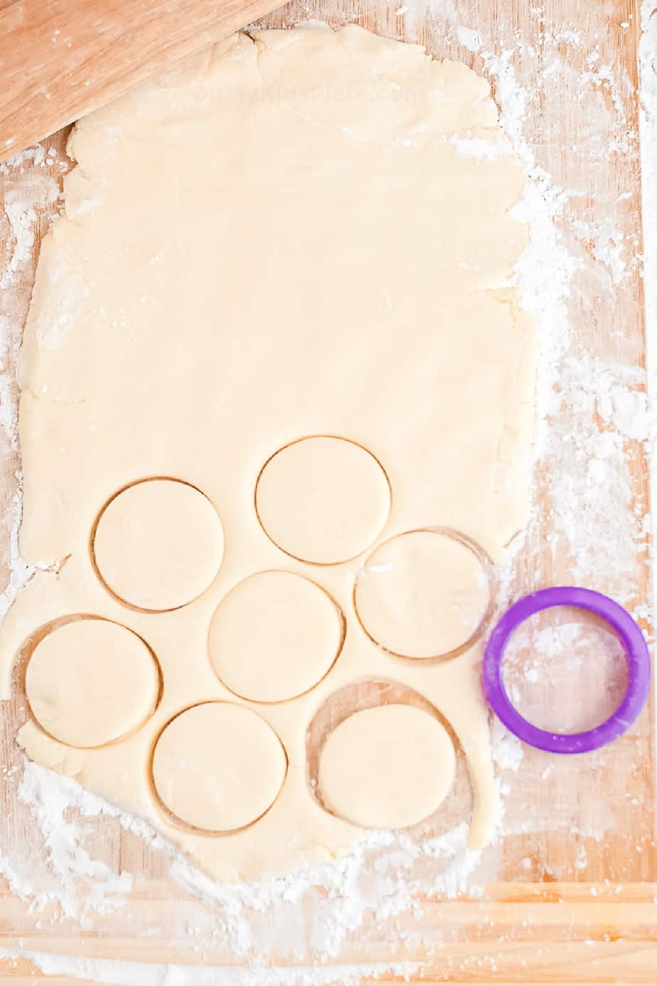 Peppermint candy dough rolled on a cutting board being sliced with a cookie cutter