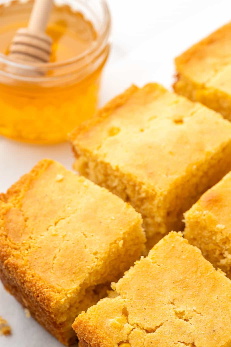 An angled view of cornbread sliced with a jar of honey in the background