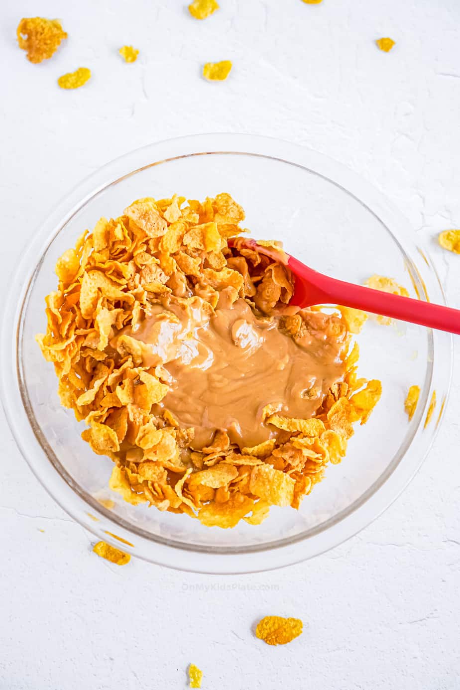 Cornflakes and peanut butter mixture mixing together in a bowl with a spatula
