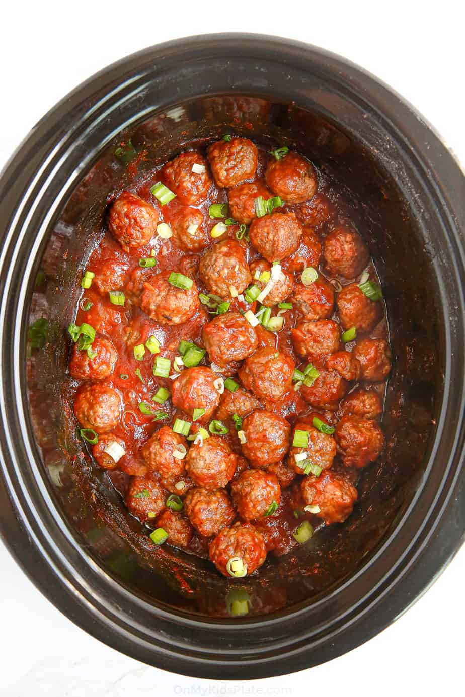 Meatballs in red sauce from overhead in the slow cooker with green onions.