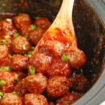 meatballs close up in a red sauce being lifted from a slow cooker by a spoon