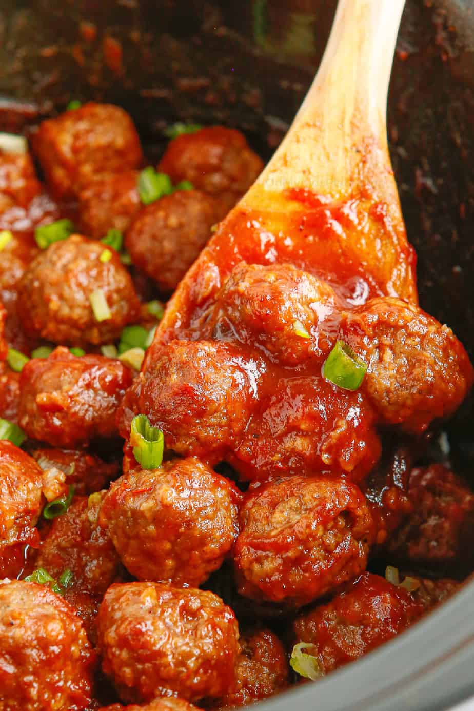 close up of a spoon lifting meatballs in red sauce out of the slow cooker
