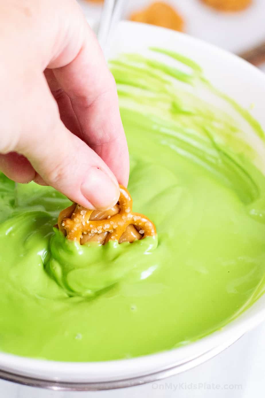 Close up of a pretzel with caramel being dipped in a bowl full of green candy melts