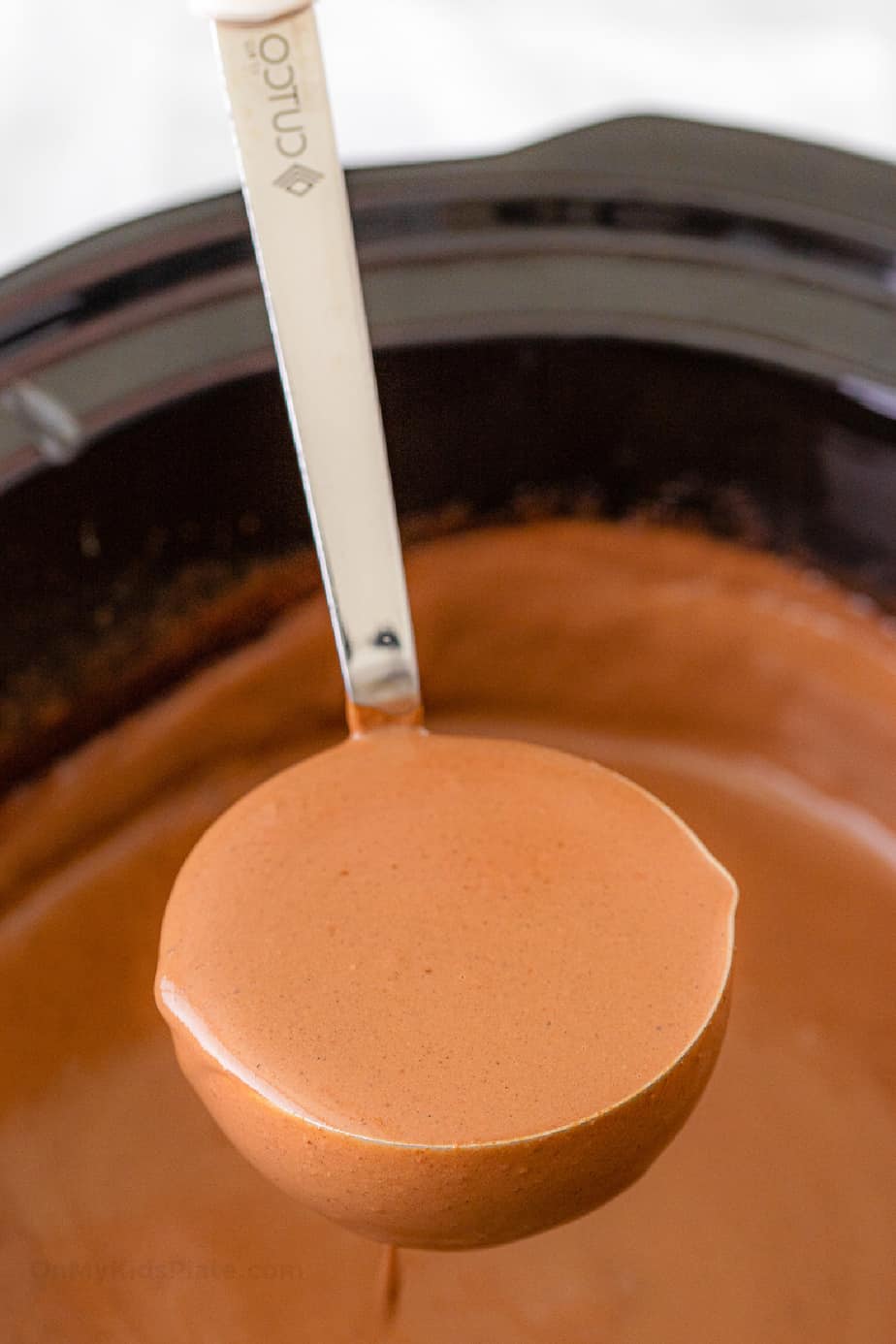 A ladle of creamy hot chocolate being lifted from a slow cooker