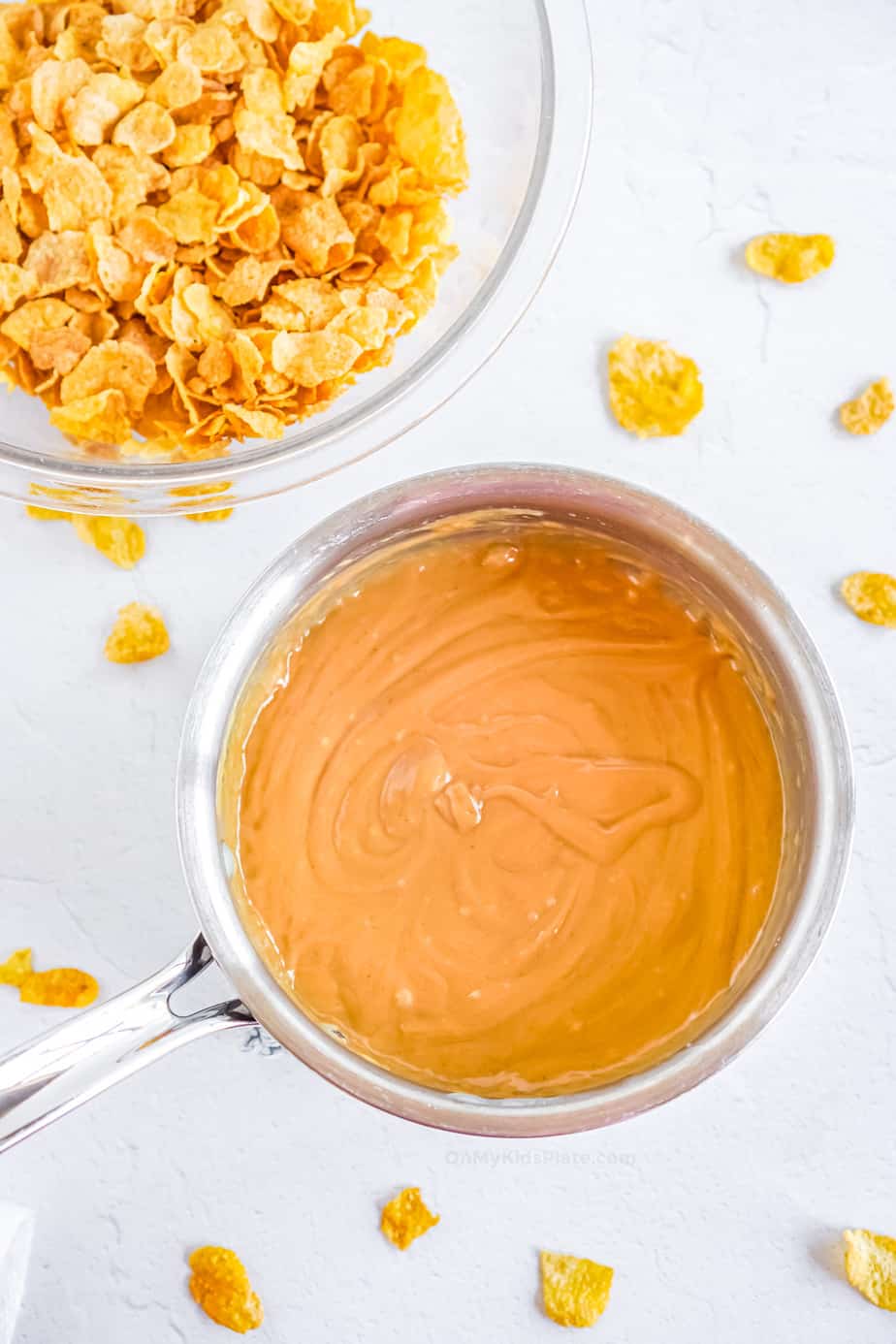 Peanut butter mixture melted in pan with cornflakes in a bowl next to it