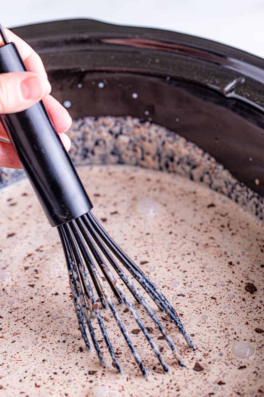 Close up blending hot chocolate in a slow cooker with a whisk