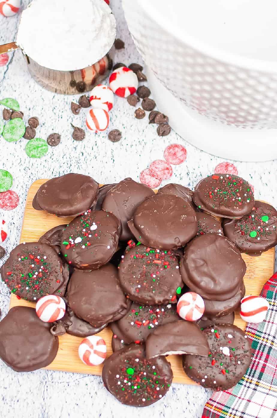 Stacks of peppermint patties dipped in chocolate on a cutting board with other peppermint candies on a cutting board.