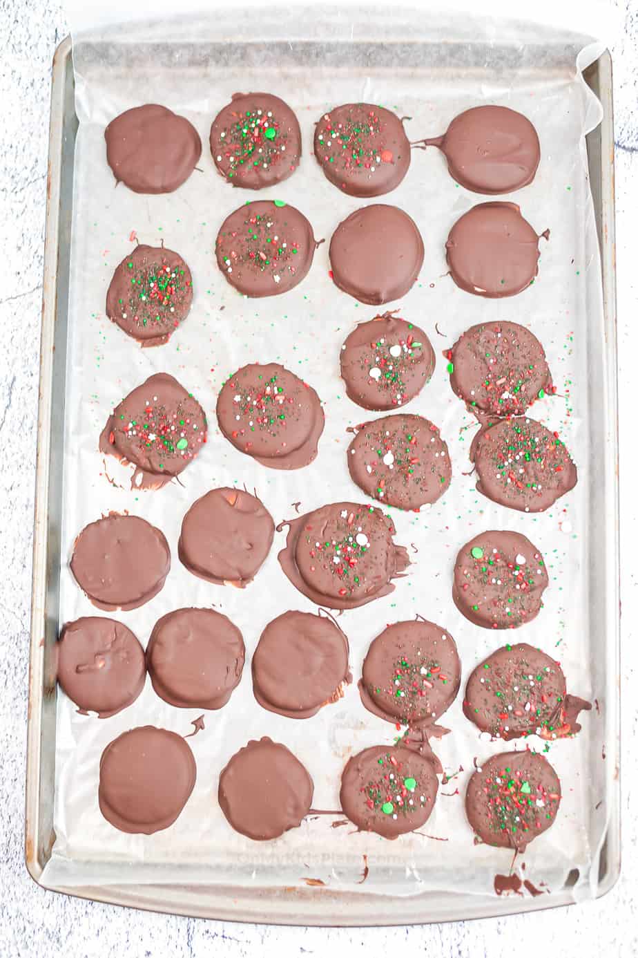 Peppermint patty candies dipped in chocolate on a baking pan, some topped with sprinkles