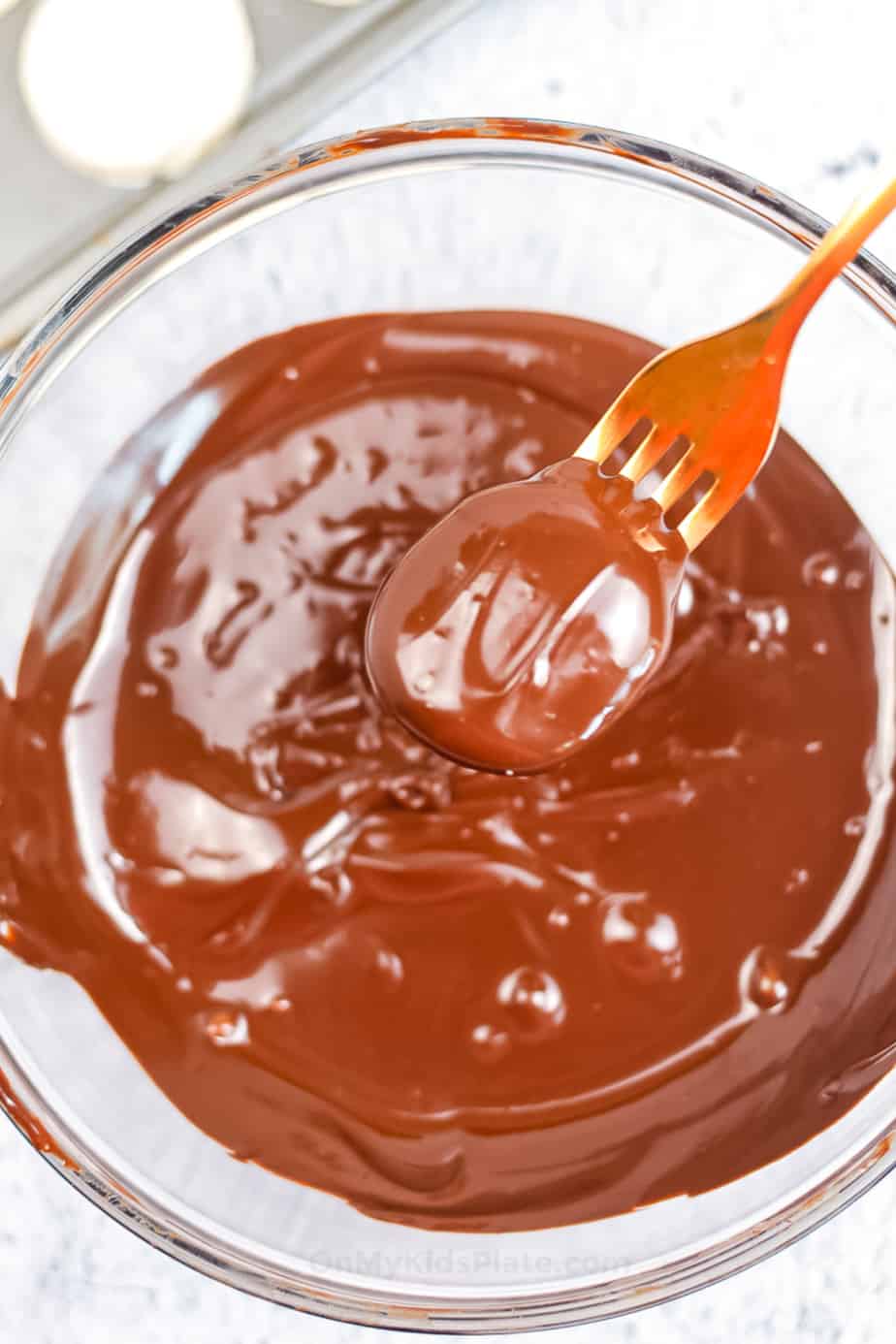 One peppermint candy being dipped in a bowl of chocolate with a fork