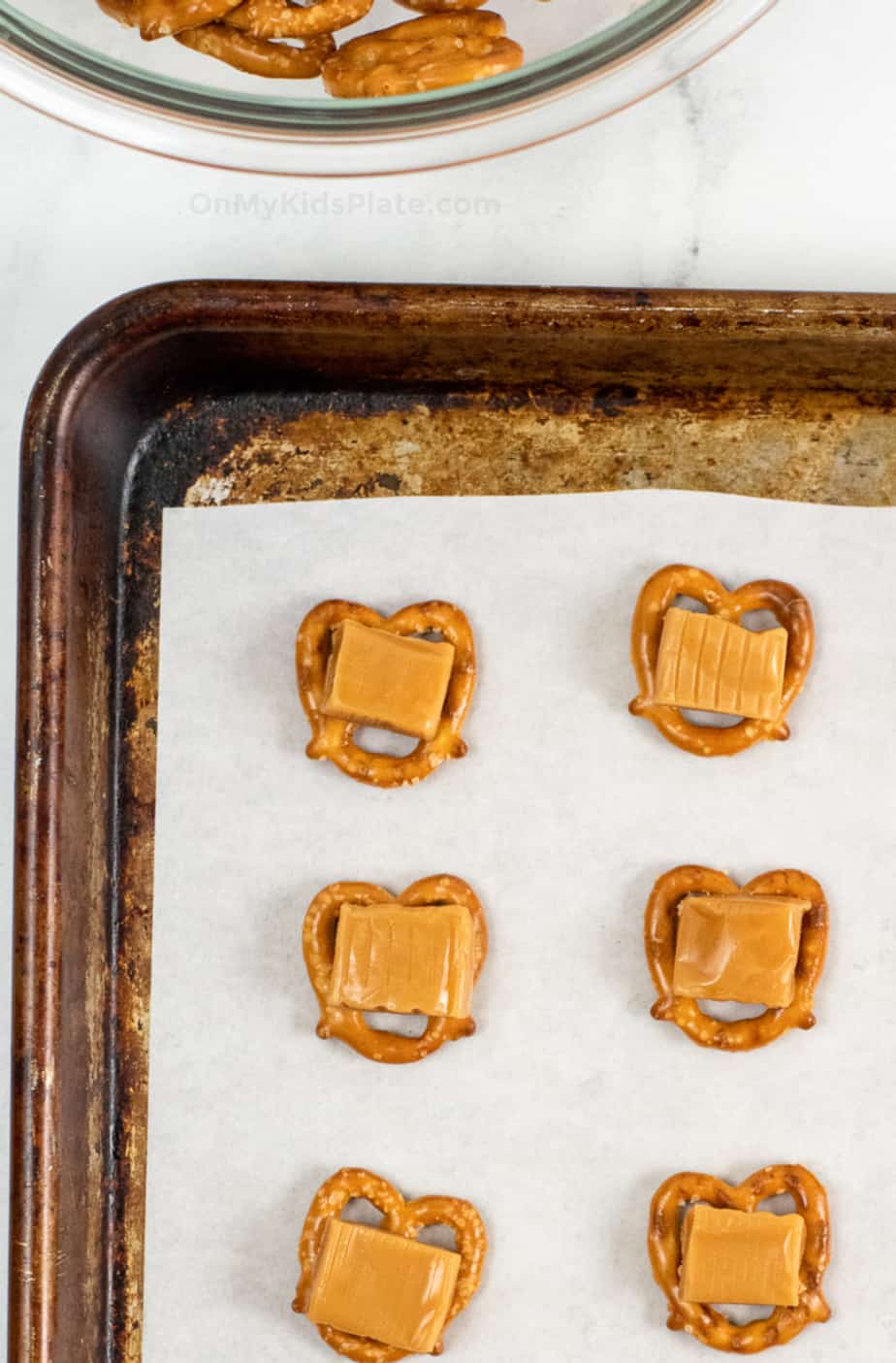 Close up of a pan covered in pretzels topped with a piece of caramel on each pretzel.