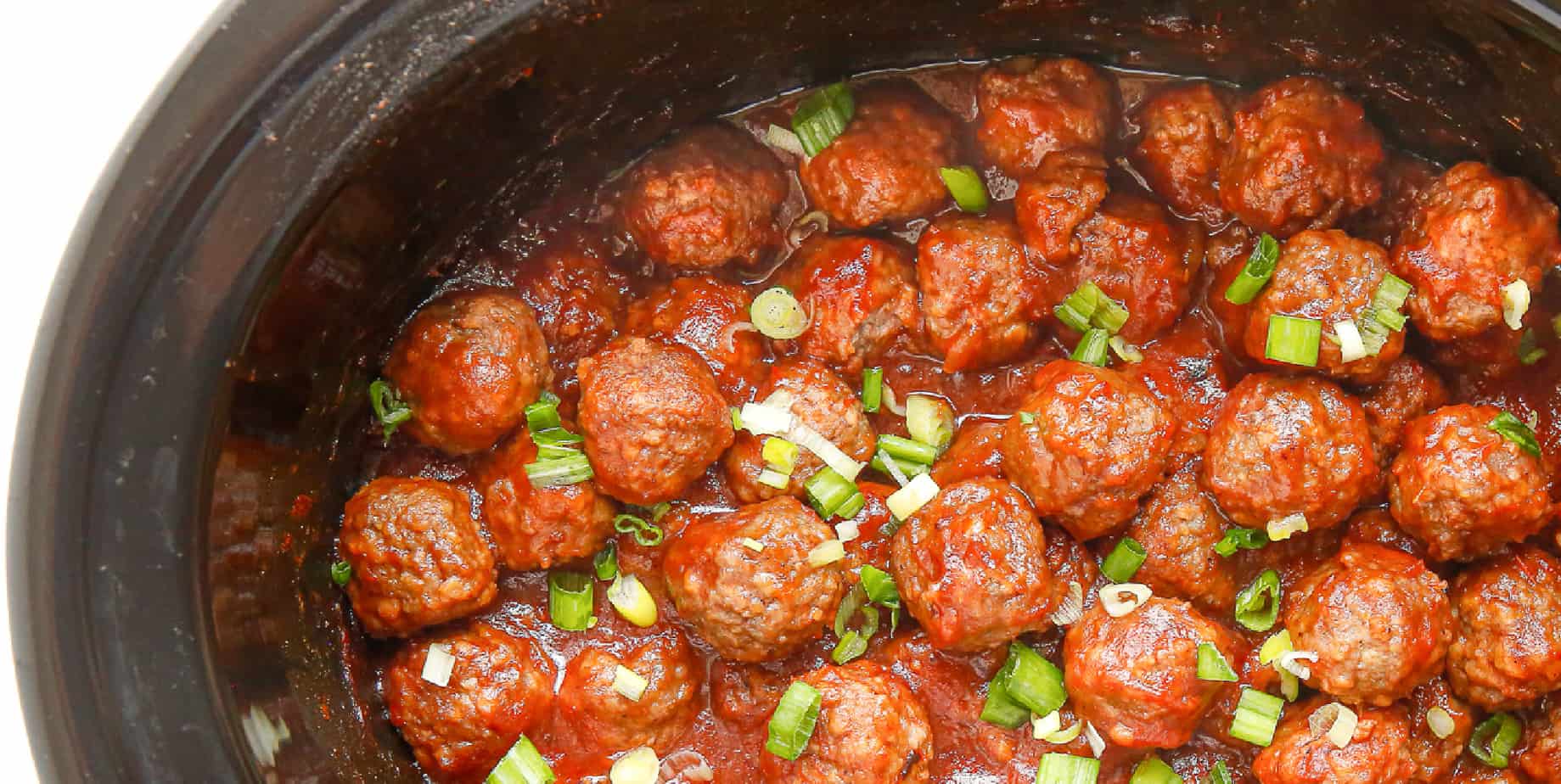 Cranberry meaballs in a slow cooker from overhead with green onions scattered on top.