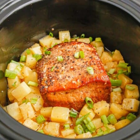 Close up view inside a slowcooker with cooked pork loin and pineapple