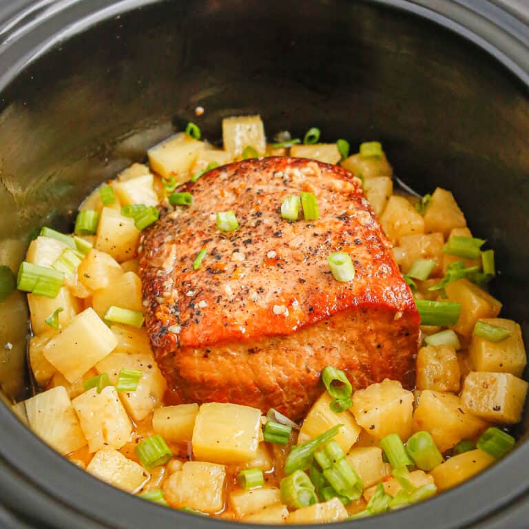 Close up view inside a slowcooker with cooked pork loin and pineapple