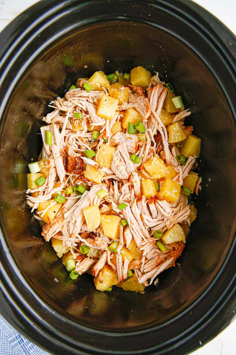 Shredded pork in slow cooker mixed with pineapple pieces