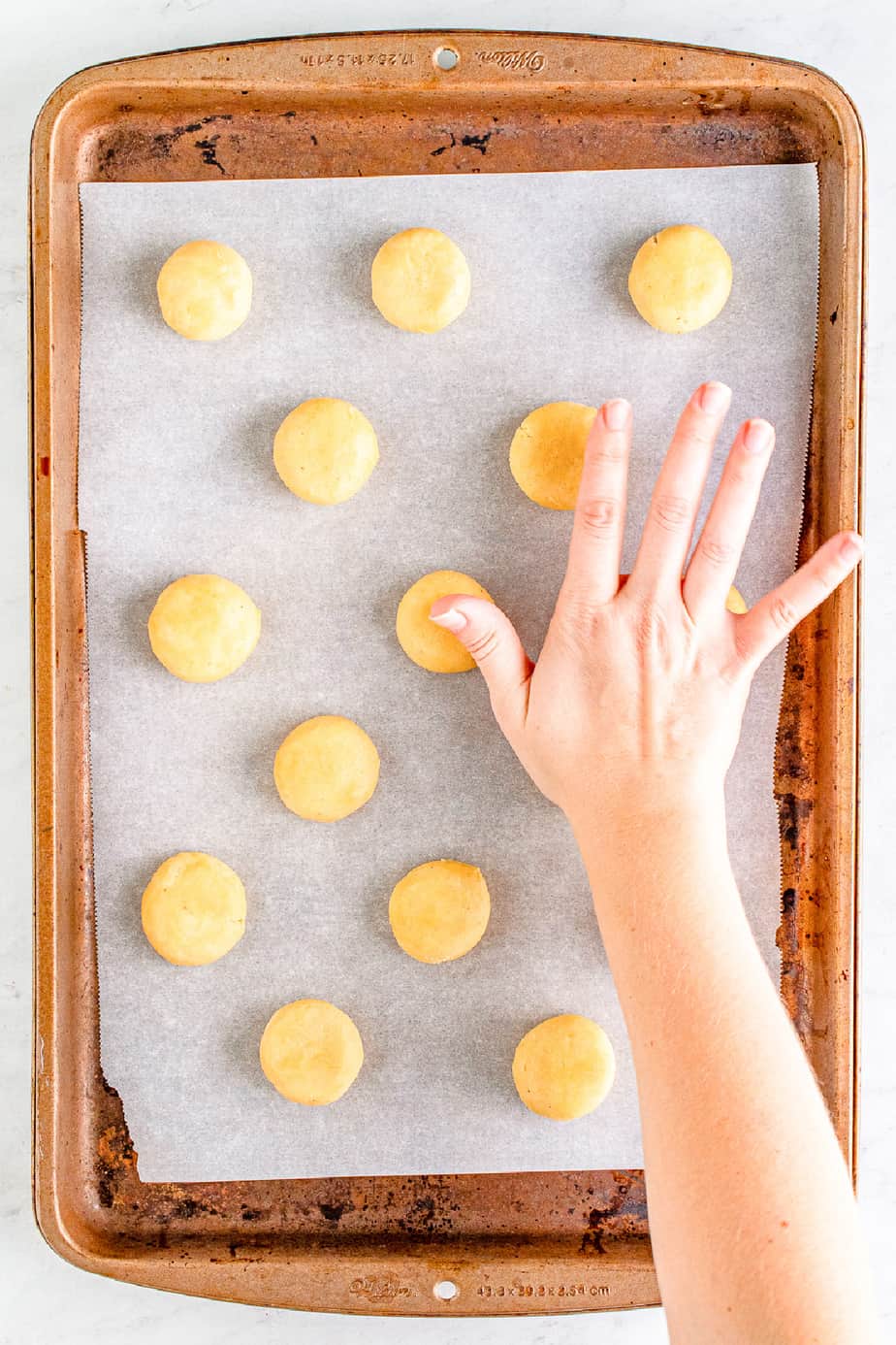 Hand pressing the tops of eggnog cookies to flatten the dough balls on a baking pan