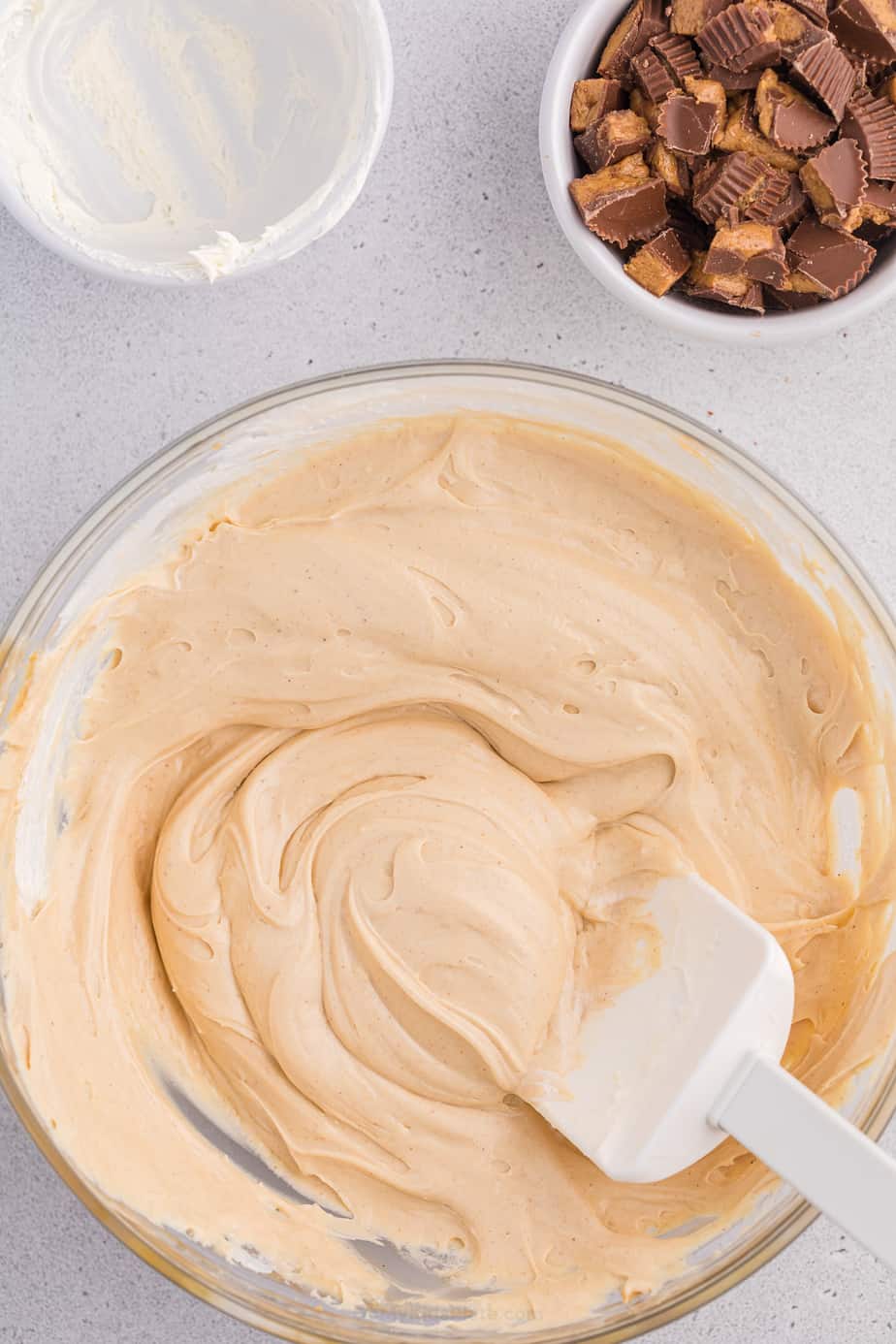 Whipped topping folded into cheesecake dip in a bowl with a bowl of chopped peanut butter cups nearby