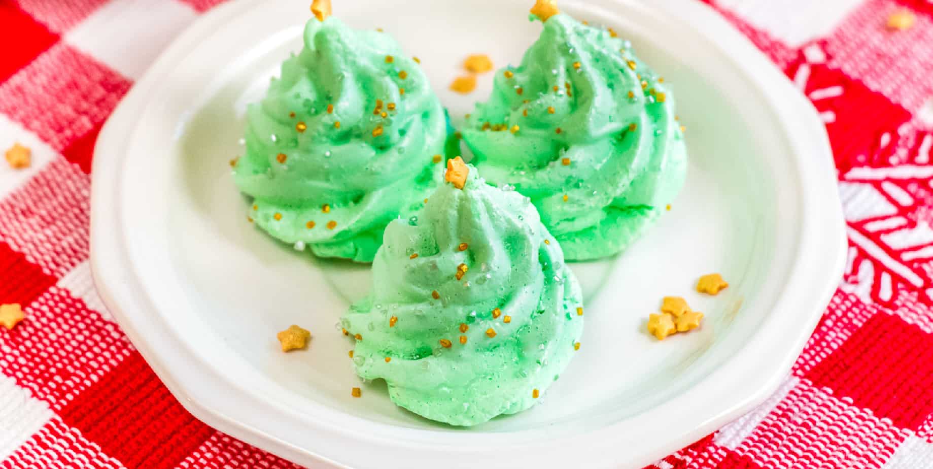 Three green christmas tree meringue cookies decorated with sprinkles on a plate