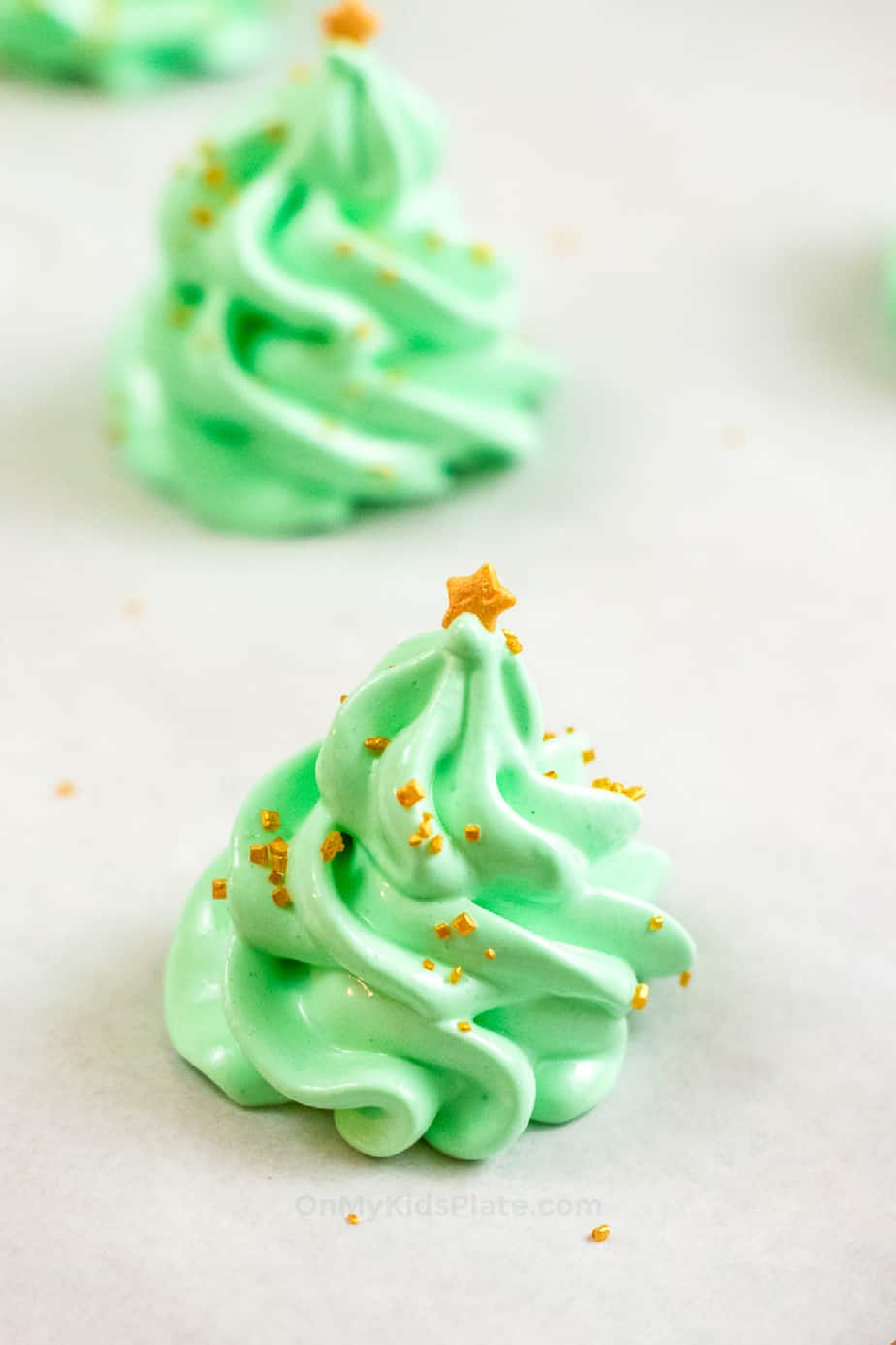 Close up side view of green meringue decorated like christmas trees with sprinkles and a star