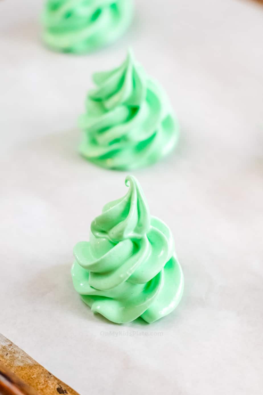 Green meringue piped into a christmas tree shape on a parchment lined baking sheet from the side