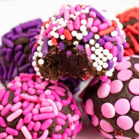 Close up of brownie truffles in a small stack with one missing a bite. Treats have pink, red and purple sprinkles