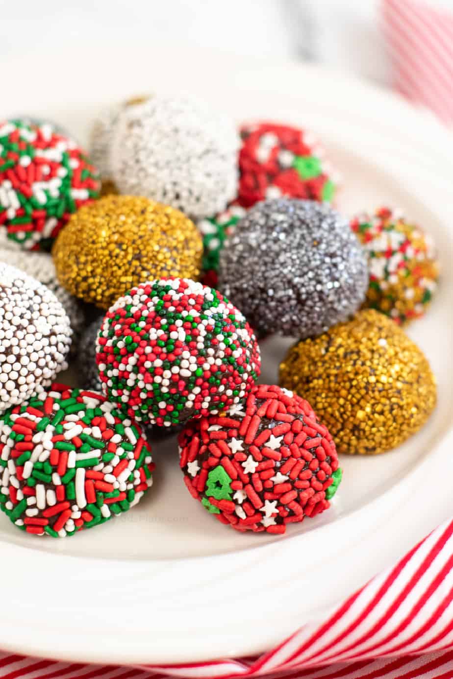 Chocolate brownie truffles piled high on a plate rolled in Christmas themed sprinkles