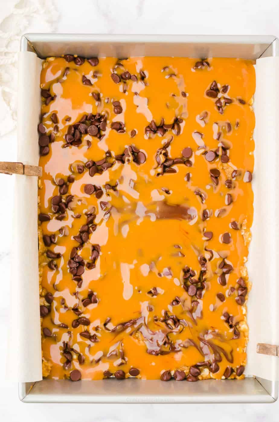 Caramel and chocolate chip layer being added to Carmelita bars in pan
