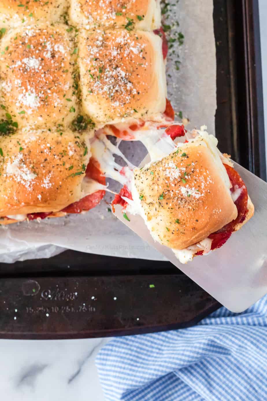 Cheesy pizza slider being pulled from pan with spatula