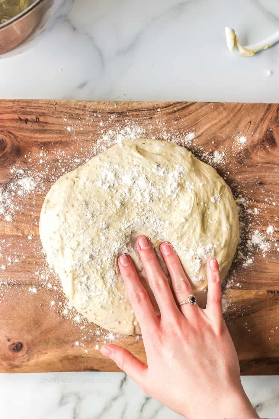 Hand touching pizza dough to roll it out