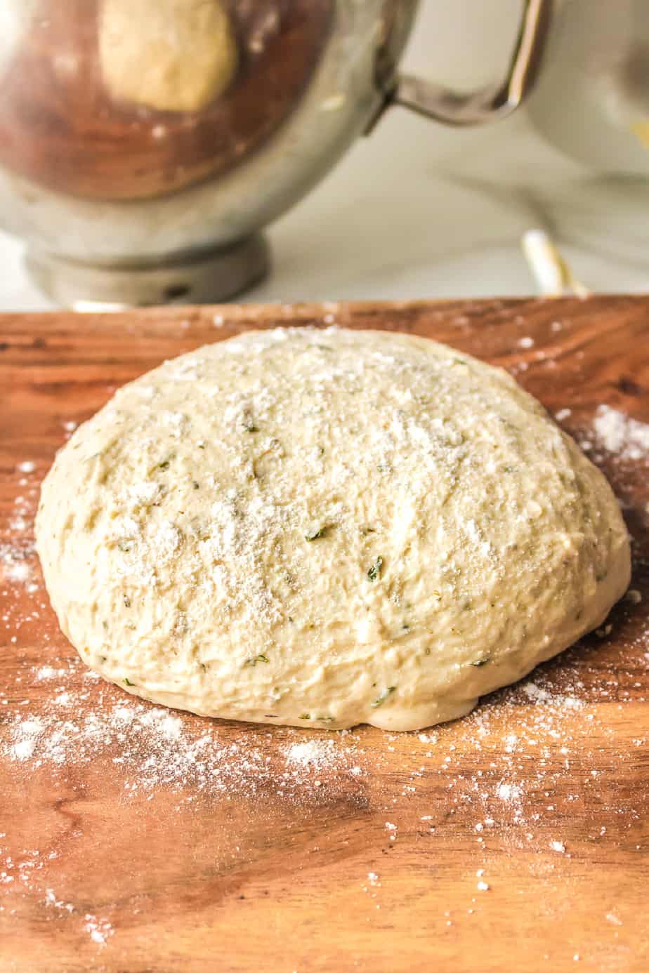 homemade pizza dough ball on a cutting board with a stand mixer bowl behind