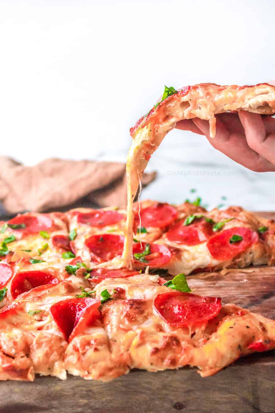 A hand pulls a slice of pizza up from a full pie with the melted cheese stretching