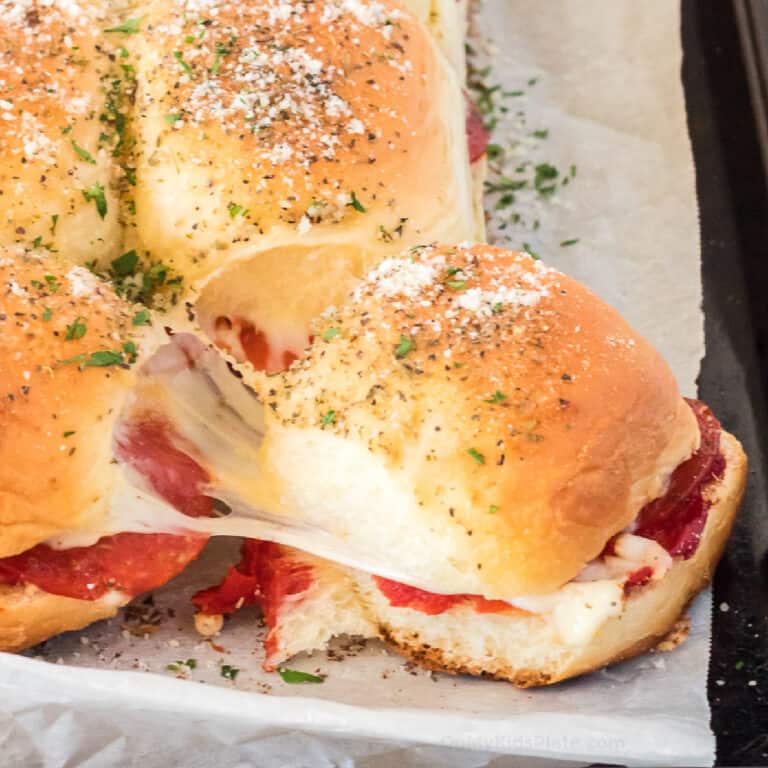 Cheesy pizza slider being pulled apart from the other sandwiches on the pan