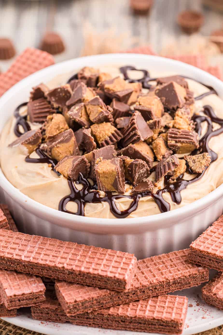 Cheesecake dip in a bowl covered in chocolate syrup and chopped peanut butter cup with cookies on a platters