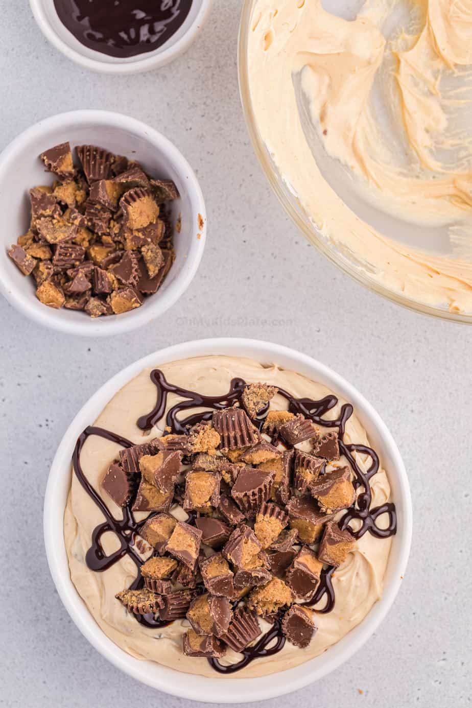 Cheesecake dip in a bowl overhead topped with peanut butter cups and chocolate. Ingredient bowls next to the dip