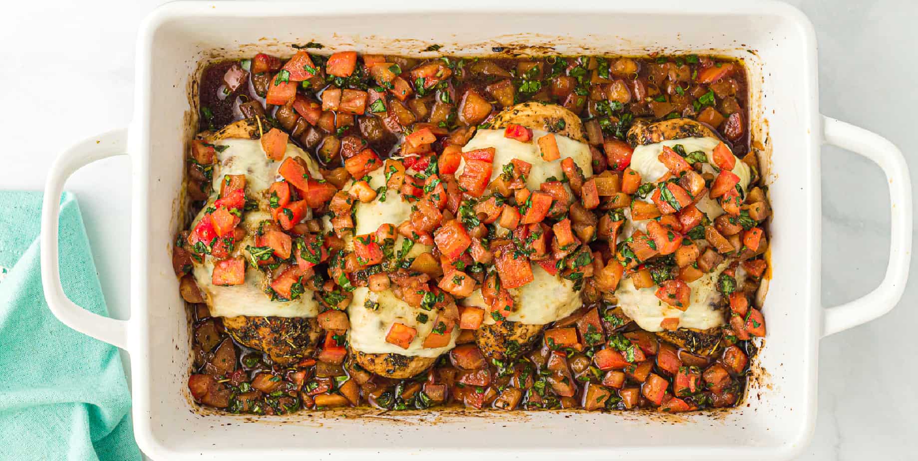 Pan of baked chicken covered in diced bruschetta tomatoes and cheese from above.