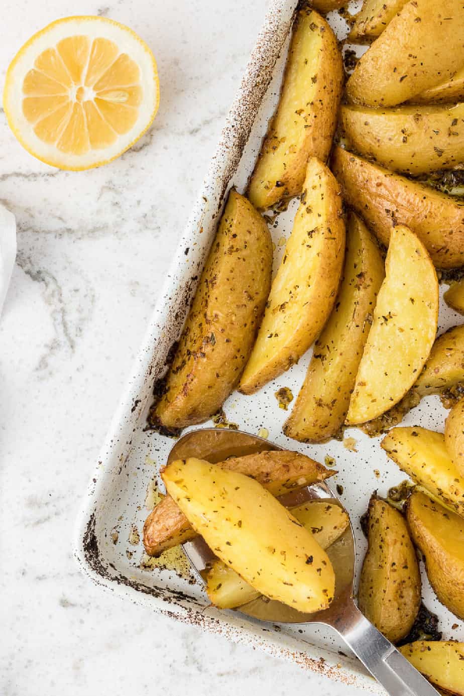 greek potato wedges roasted on the pan with fresh lemon nearby