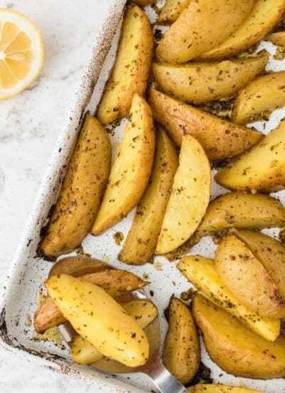 Greek potatoes roasted on the pan with a lemon on the counter next to the pan