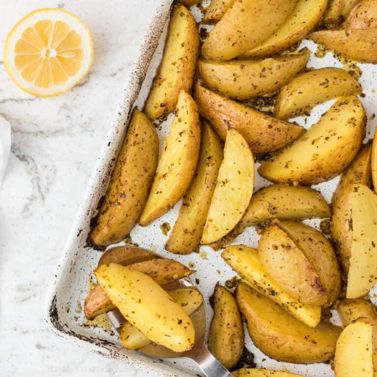 Greek potatoes roasted on the pan with a lemon on the counter next to the pan