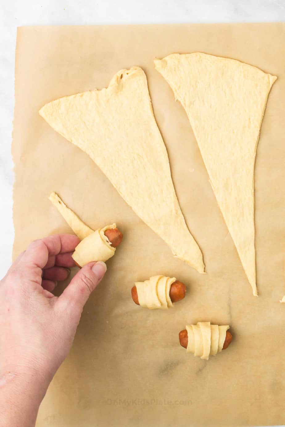 Rolling small sausages in pieces of crescent roll dough