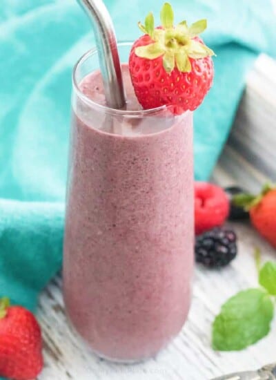close up of smoothie in a glass with berries garnishing and around the smoothie