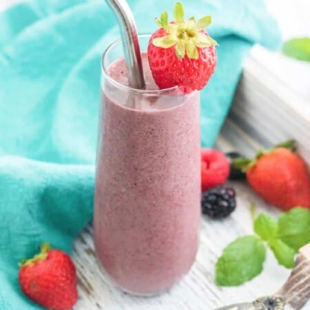 close up of smoothie in a glass with berries garnishing and around the smoothie
