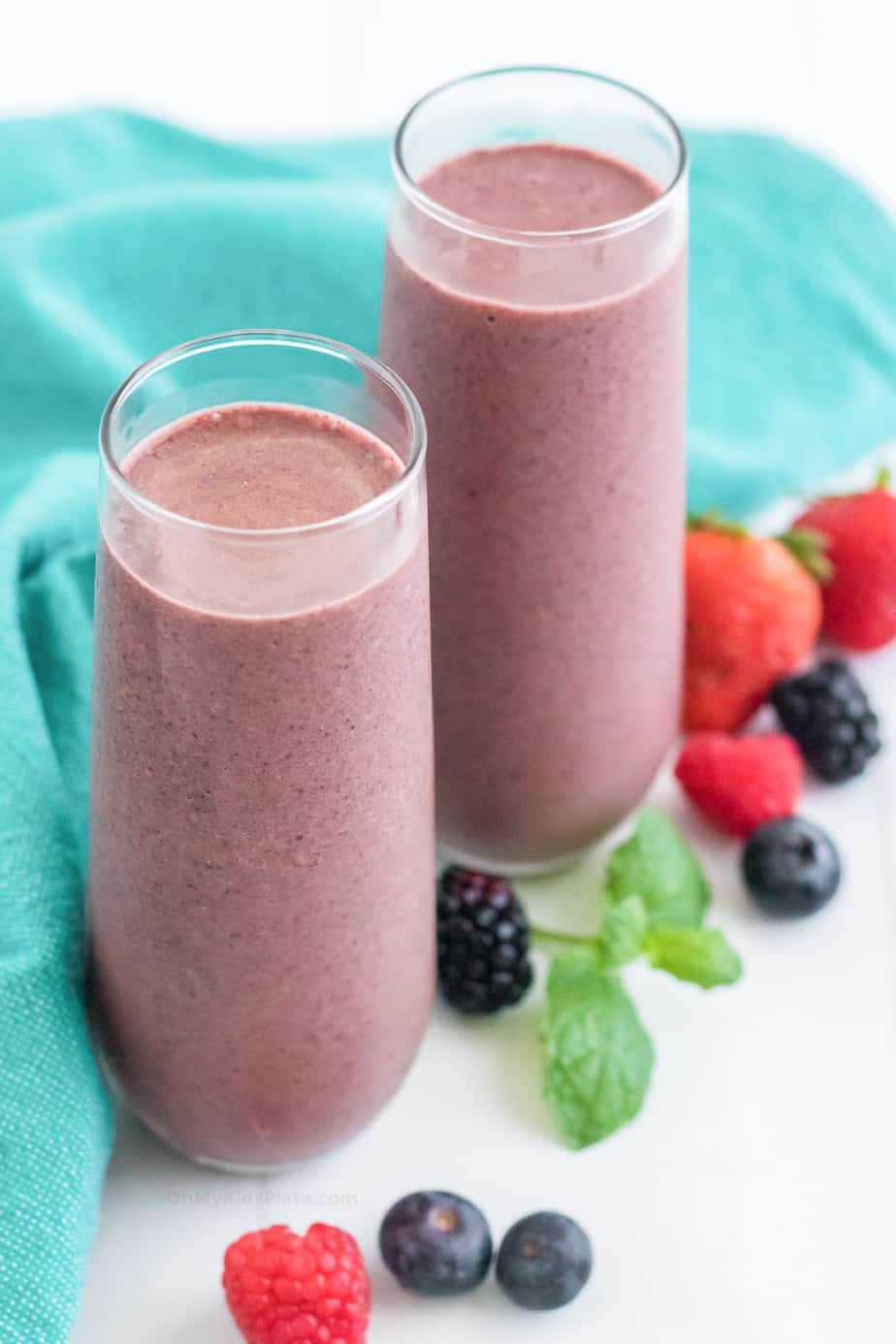 Two glasses full of smoothie with berries scattered nearby