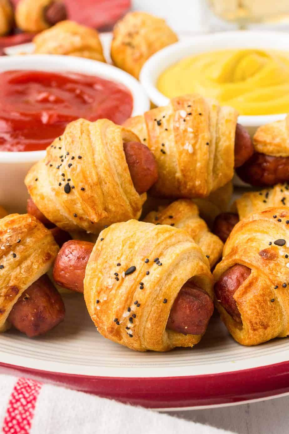 Pigs in a blanket stacked on a plate with dipping sauces in bowls behind
